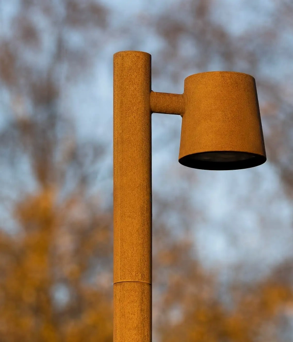 Straßenlaterne mit rundem Leuchtkörper vor einem Himmel bei Sonnenaufgang.