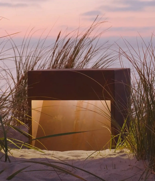 Eine moderne Außenleuchte, teilweise im Sand vergraben, umgeben von hohem Gras.