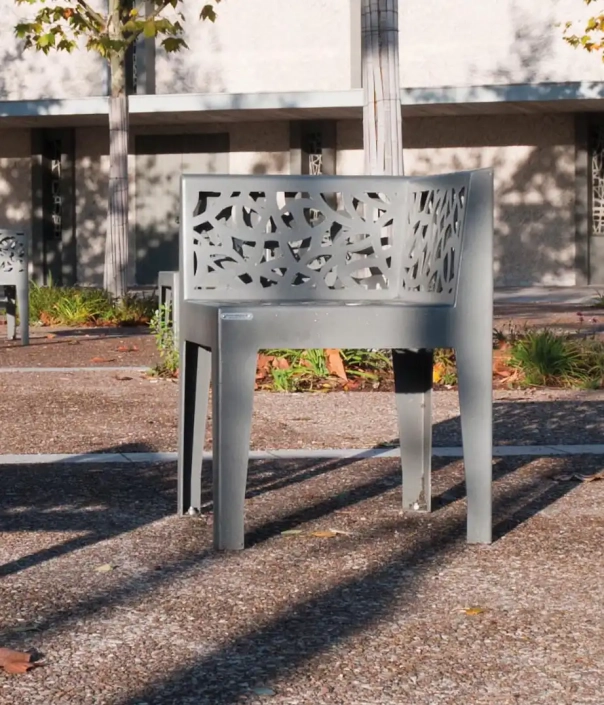 Moderner Stuhl mit filigranem Muster auf Rückenlehne und Armlehnen aus grauem Metall.