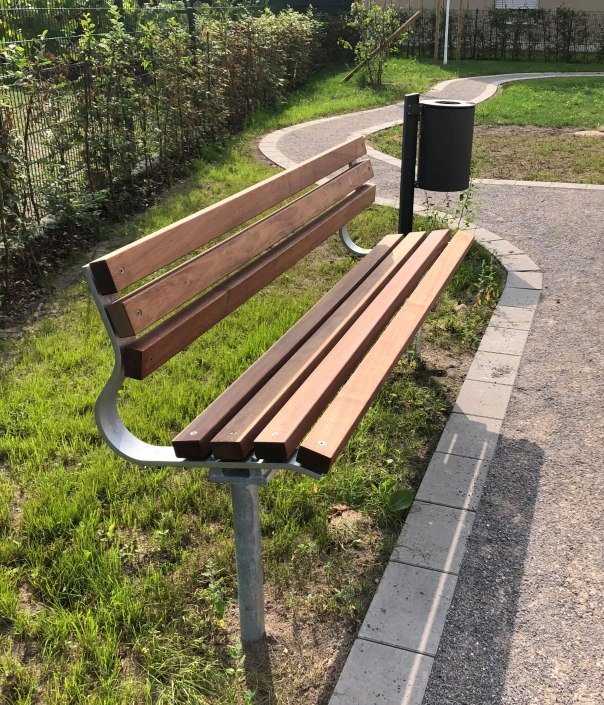 Holzbank mit Metallgestell und Abfalleimer neben einem geschwungenen Gehweg in einer Grünanlage.