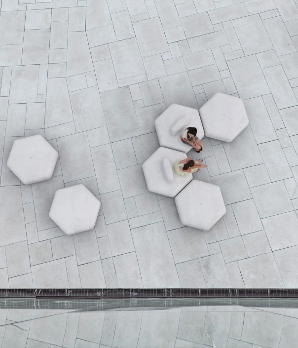 Mehrere hexagonale Sitzmöbel aus weißem Beton auf einem grauen Pflasterboden, mit zwei Personen, die auf einem der Möbelstücke sitzen.