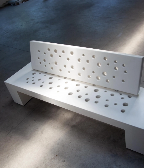 Weißes Bankdesign aus Beton mit kreisförmigen Löchern in der Rückenlehne und Sitzfläche.