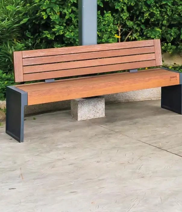 Holzbank mit Rückenlehne und Metallgestell in einer begrünten Umgebung.