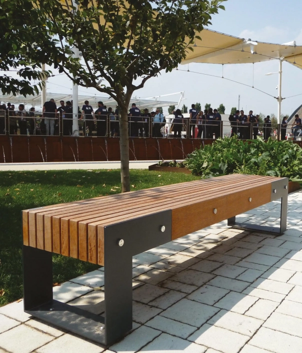 Holz- und Metallbank in einem öffentlichen Parkbereich unter einem schattenspendenden Baum.