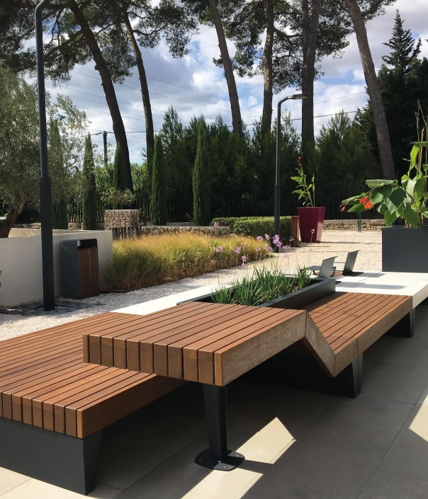 Moderne Sitzlandschaft aus Holz und Metall mit integrierten Pflanzkästen in einer parkähnlichen Umgebung.