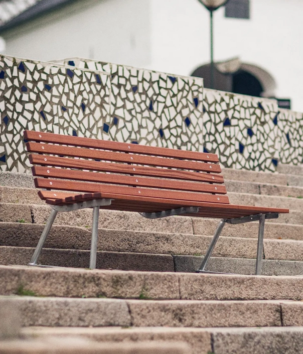 Eine Holzbank steht auf einer Treppe, umgeben von einem mosaikartig gestalteten Hintergrund.