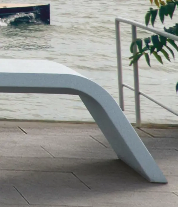 Ein modernes, geschwungenes Bankdesign steht an einem Gewässer, umgeben von einem Gehweg und Pflanzen im Vordergrund.