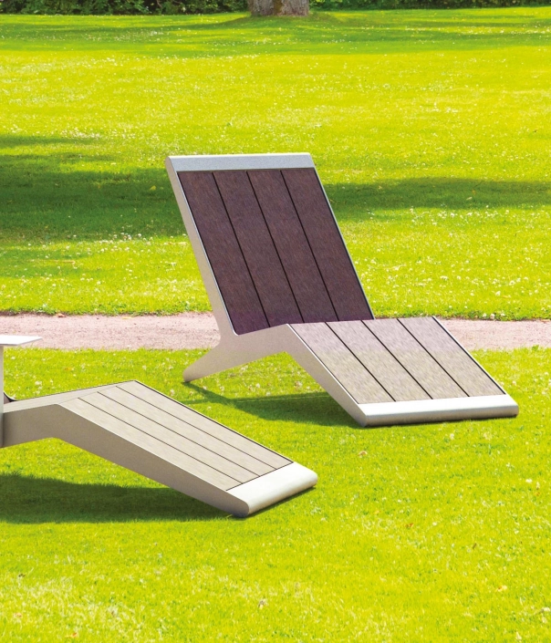 Mehrere moderne Outdoor-Liegen mit Holzlatten und Metallgestell in einem Park mit grüner Wiese und Bäumen.