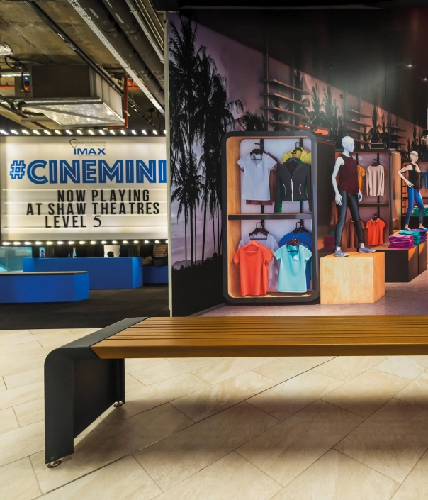 Blick auf eine moderne Holzbank mit schwarzem Metallgestell, die in einem stilvollen Innenraum steht. Im Hintergrund sind Kleidung und Accessoires sichtbar.