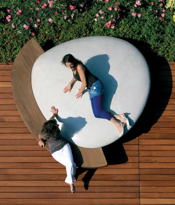 Moderne Sitzlandschaft mit großer Steinbank und Holzplattform, auf der zwei Personen entspannen.