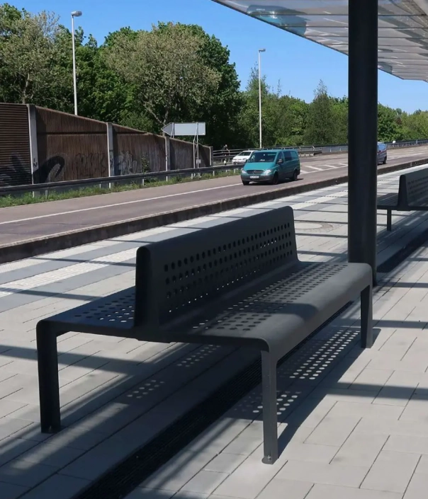Dunkle Metallbank mit perforierter Rückenlehne an einer modernen Haltestelle.