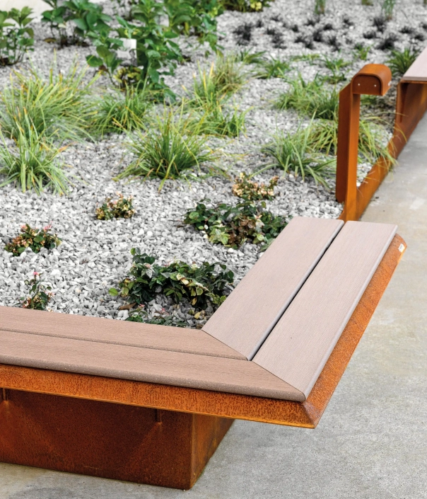 L-förmige Sitzbank mit rostfarbener Metallbasis und Holzsitzfläche in einem modernen Kiesgarten.
