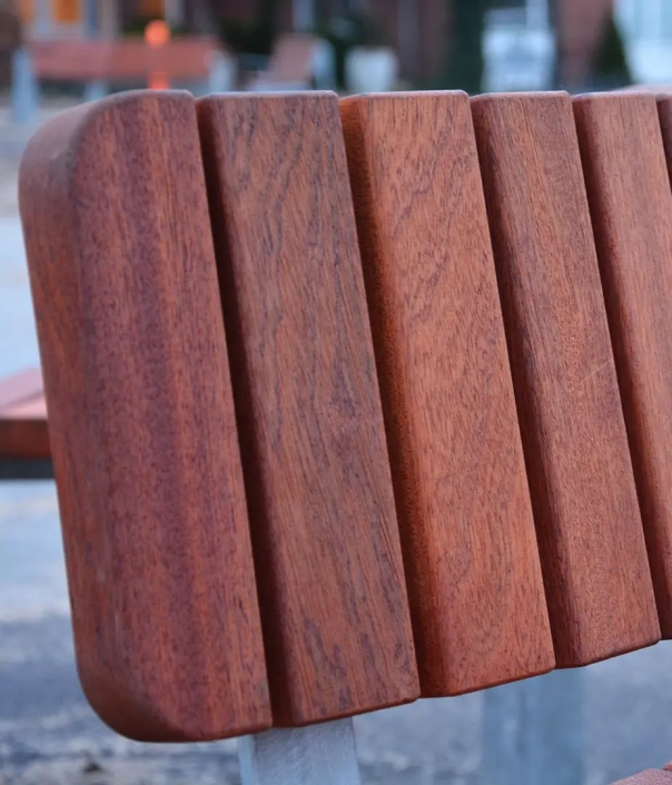 Alt-Text: Nahaufnahme einer Holzbank mit einem strukturierten, schlichten Rücken. Die Bank zeigt eine warme, natürliche Holzfarbe und eine moderne Form.