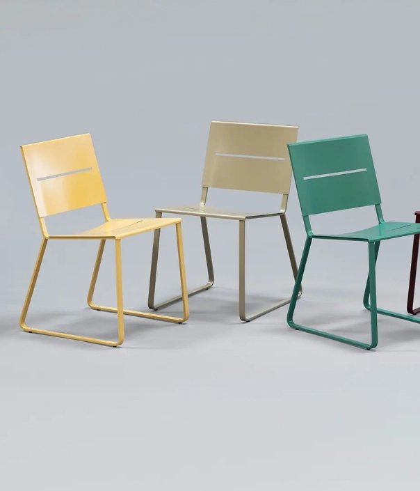 Vier moderne Stühle in verschiedenen Farben (gelb, beige, grün und rot) stehen auf einem grauen Untergrund.