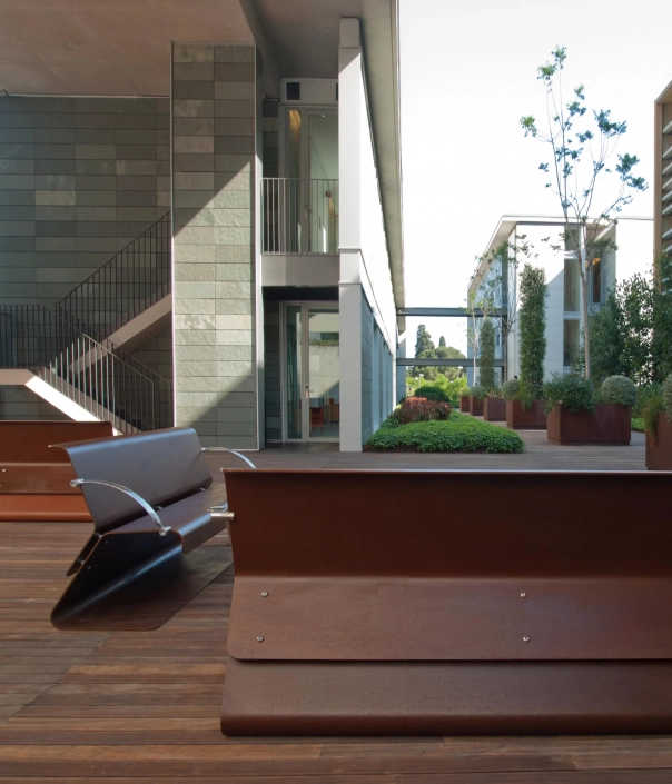 Bild eines modernen Innenhofs mit Holzterrasse, Sitzbänken und begrünten Töpfen, umgeben von zeitgenössischer Architektur.