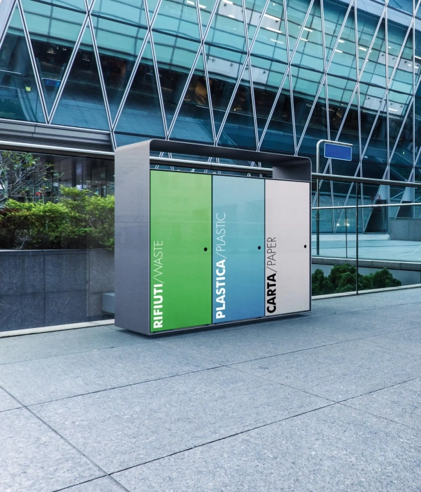 Modernes Recycling-Möbel mit drei großen Fächern für Restmüll, Plastik und Papier, platziert vor einer Glasfassade eines Gebäudes.