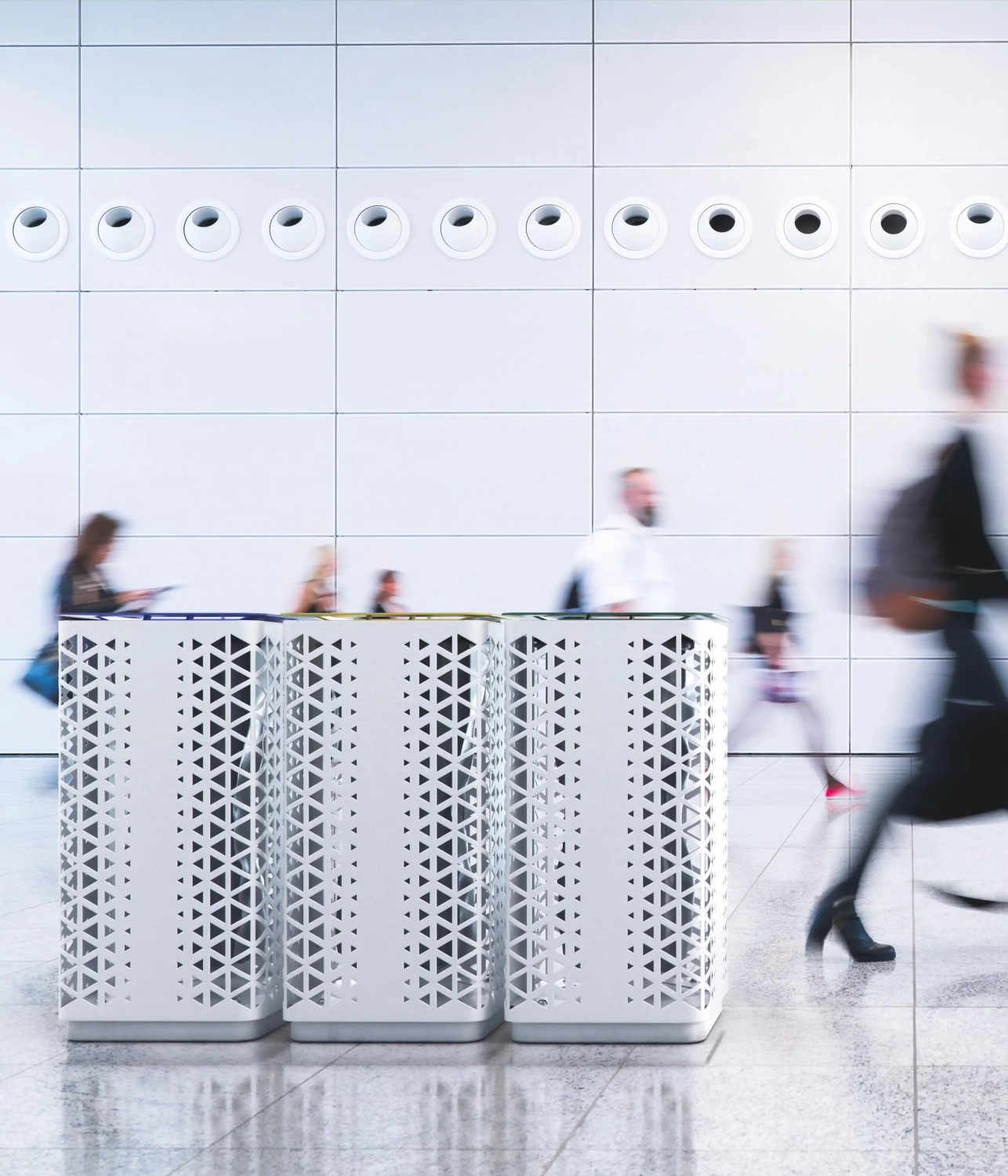 Drei moderne, geometrisch gestaltete Müllbehälter stehen vor einer hellen Wand mit runden Lüftungsschlitzen.