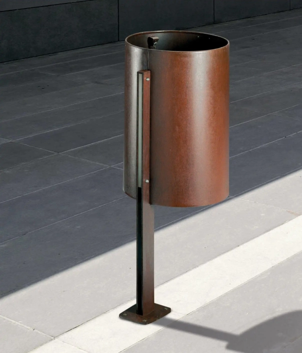 Moderner Abfallbehälter aus metallischem Material, in Zylinderform, auf einem grauen Pflasterboden.
