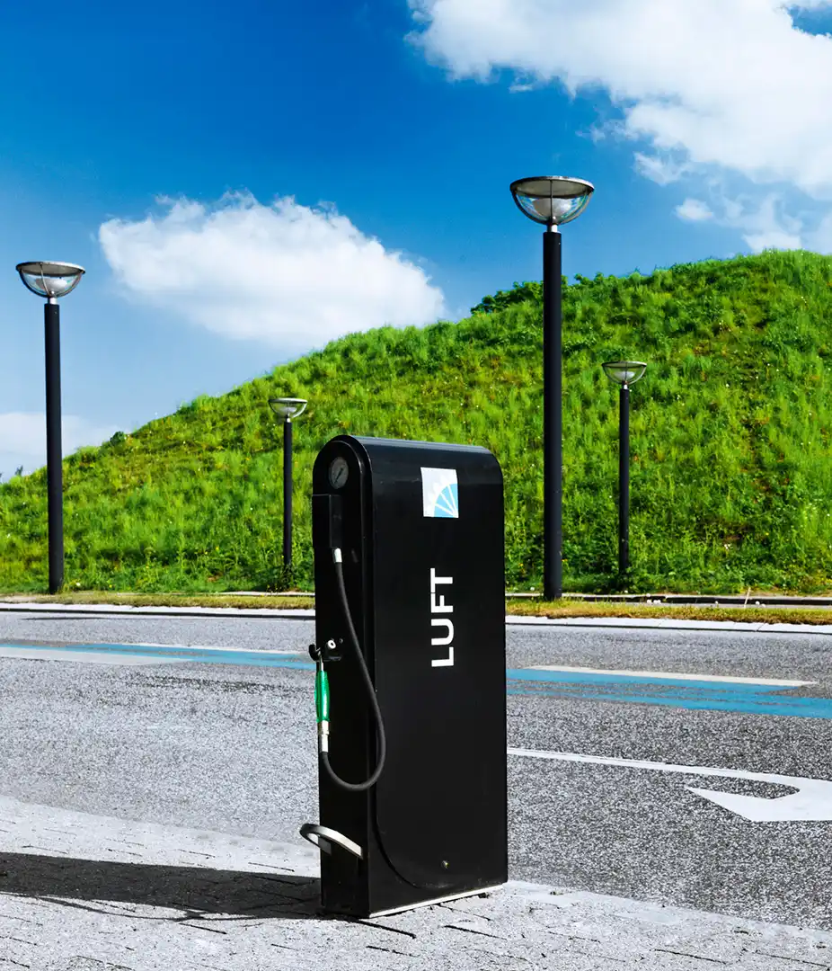 Alt-Text: "Öffentliche Fahrradluftpumpe in einer urbanen Umgebung mit grüner Landschaft im Hintergrund."