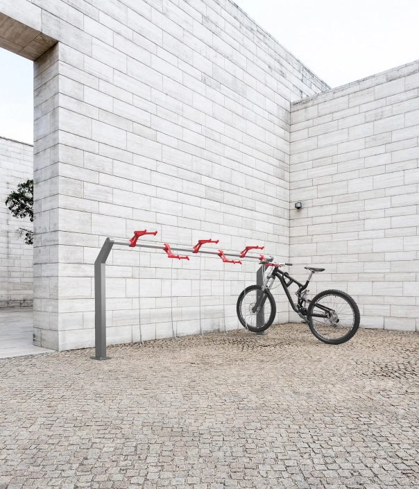 biella-radverkehr-09 Alt-Text: "Moderne Fahrradabstellanlage mit roten Fahrradständern und einem Mountainbike in einem minimalistischen Innenhof."