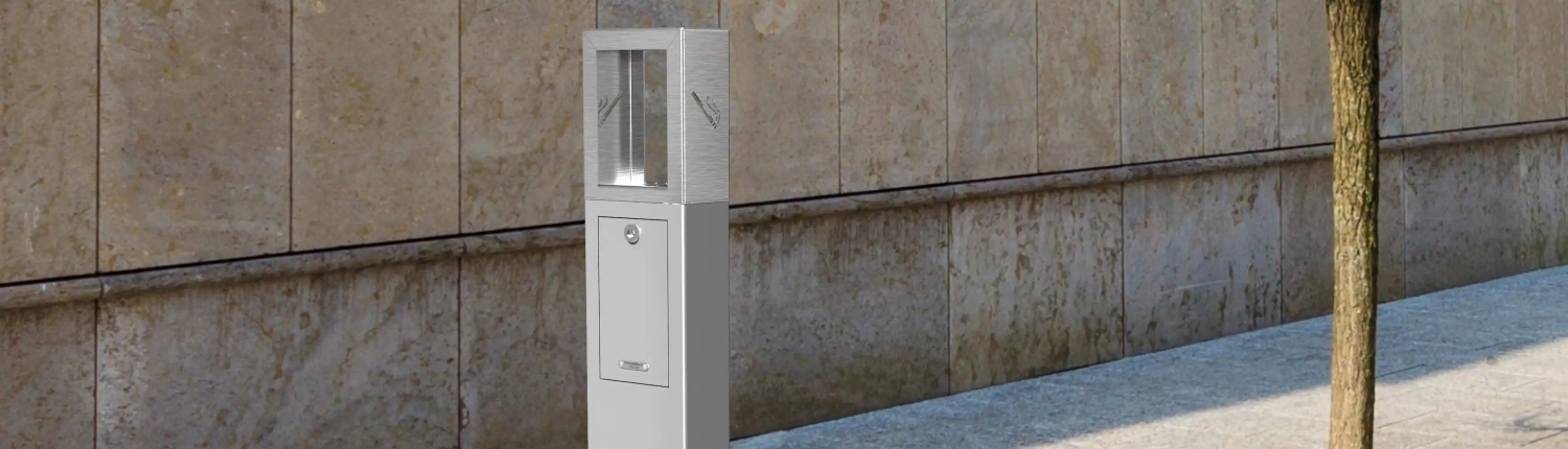 Alt-Text: Moderner, silberner Ascher auf einem Gehweg, vor einer Steinwand platziert.