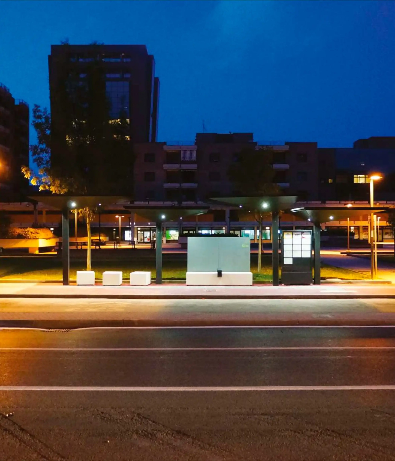 Alt-Text: Moderne Überdachung an einer Haltestelle bei Nacht, mit beleuchtetem Wartenbereich und urbaner Umgebung.