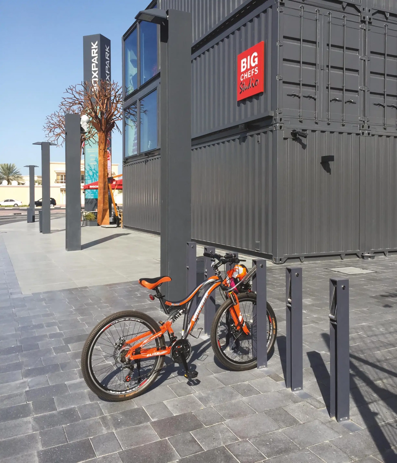 Alt-Text: "Fahrradständer mit einem geparkten orangefarbenen Fahrrad vor einem modernen Gebäude."