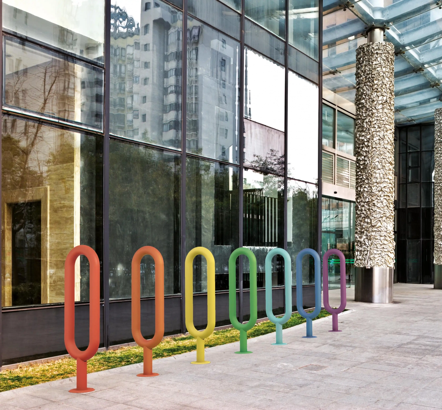 Alt-Text: Eine Reihe bunter Fahrradständer in modernem Design, auf einem gepflasterten Gehweg vor einem Glasgebäude platziert.