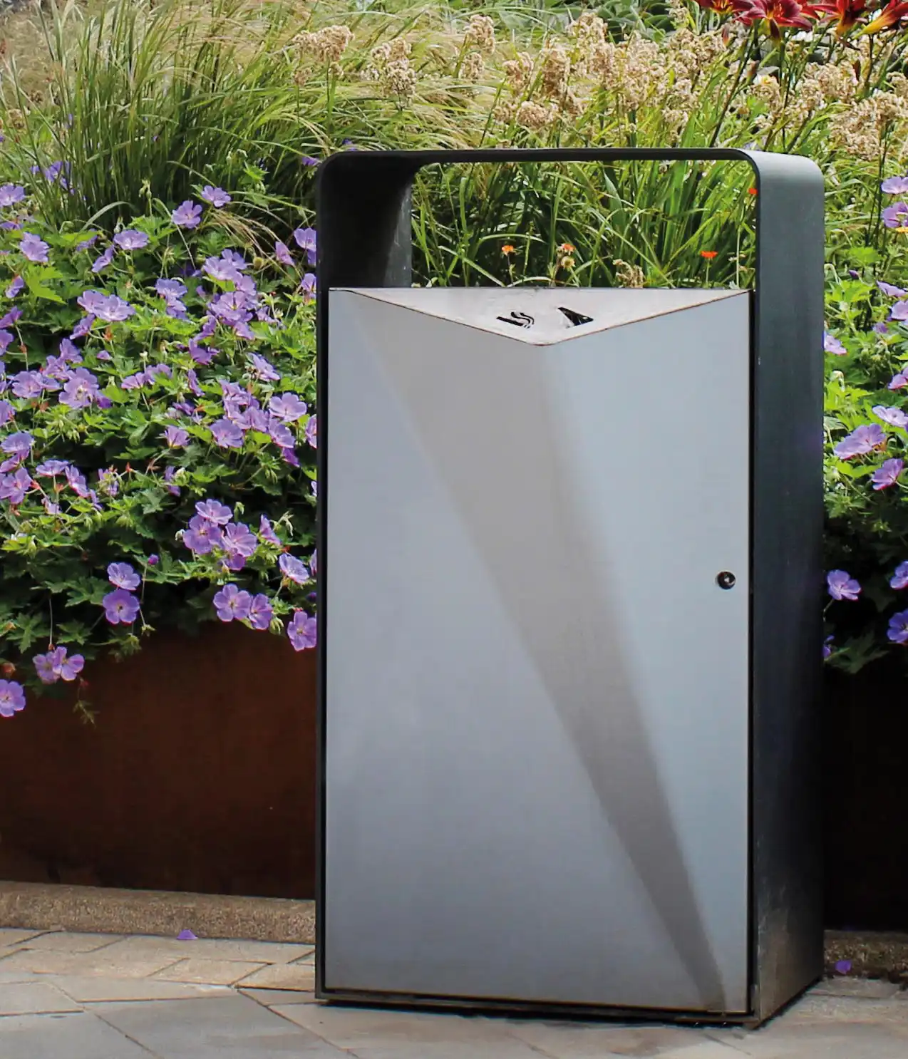 Moderne Abfalltonne in einem bepflanzten Garten mit bunten Blumen im Hintergrund.