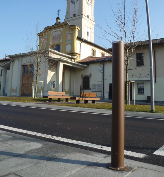 Poller in Braunfarbe vor einem Gebäude mit einer Uhrturmfassade und einer Bank im Hintergrund.
