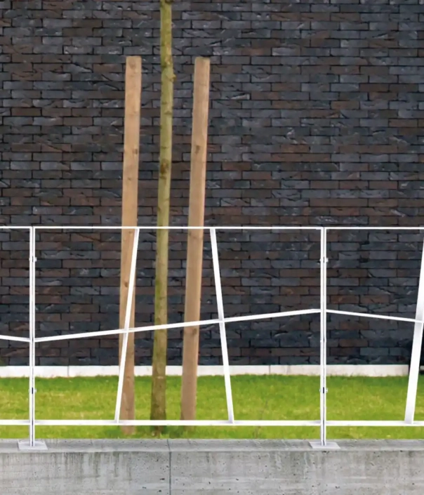 Alt-Text: „Weiße Absperrungen entlang einer Rasenfläche vor einer dunklen Steinmauer, mit Holzpfosten im Hintergrund.“