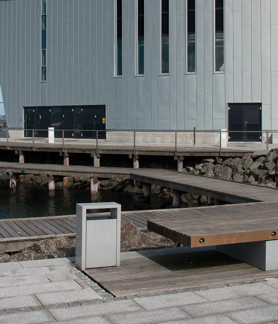 Modernes Gebäude am Wasser mit Holzstegen und einem Abfallbehälter im Vordergrund.