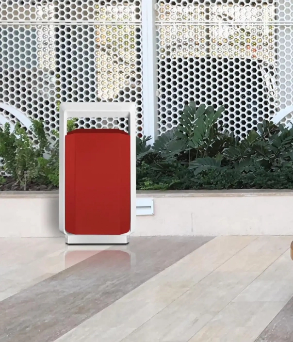 Ein moderner rot-weißer Mülleimer steht auf einem marmorierten Boden vor einem Pflanzenbeet und einem hellen, strukturierten Hintergrund.