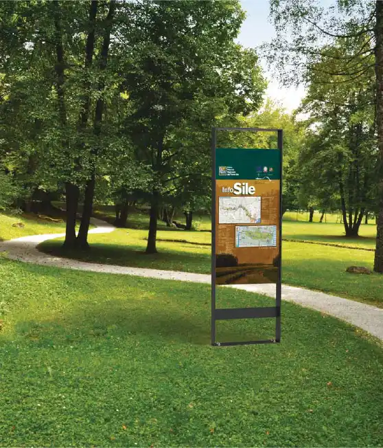 senna-hinweistafel-05 Alt-Text: Ein Hinweisschild, das Informationen und Karten in einem parkähnlichen Bereich anzeigt, umgeben von Bäumen und einer geschwungenen Fußwege.