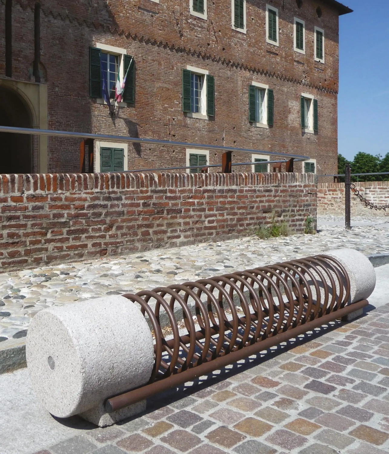 Alt-Text: "Moderner Fahrradständer aus Beton und Metall in einer städtischen Umgebung mit historischem Gebäude im Hintergrund."