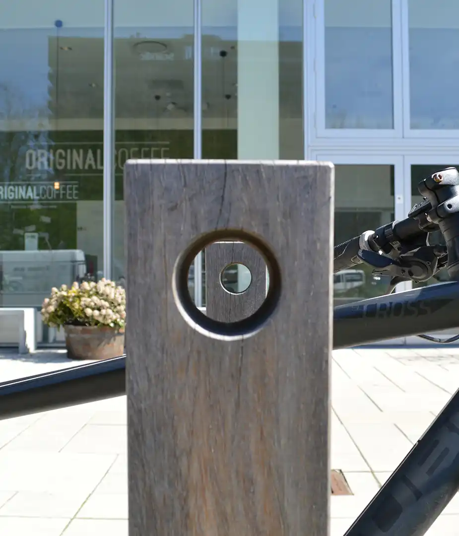 Alt-Text: "Detailansicht eines stabilen Fahrradständers mit einem Loch zum Sichern des Fahrrads, im Hintergrund ein modernes Café."