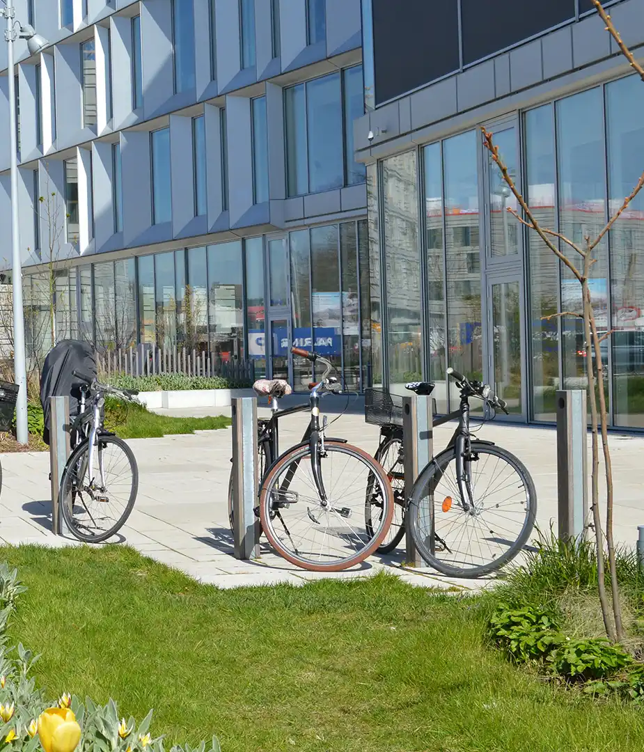 Alt-Text: "Fahrradständer mit mehreren Fahrrädern vor einem modernen Gebäude, umgeben von Rasenflächen."