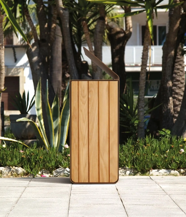 Ein moderner Mülleimer aus Holz mit einem geölten Finish steht in einem Außenbereich, umgeben von tropischen Pflanzen und Bäumen.