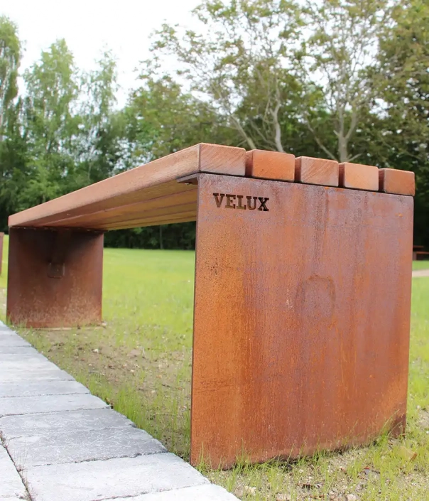 Rustikale Tisch-Bank-Kombination aus Metall mit Holzauflage, in einem grünen Park aufgestellt.